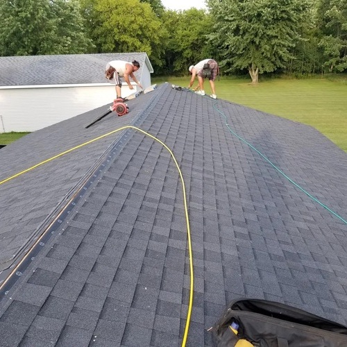 Two Roofers Install Asphalt Shingles on a Roof.